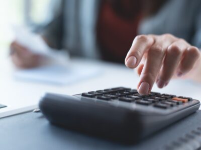 Doing finance, budgeting and tax calculation. Close up woman hand using calculator to calculate home finance, accounting with laptop computer on table, budget management, monthly expenses