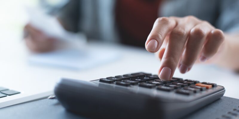 Doing finance, budgeting and tax calculation. Close up woman hand using calculator to calculate home finance, accounting with laptop computer on table, budget management, monthly expenses