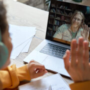 Hispanic teen girl school college student distance learning waving hand studying with online teacher on laptop screen. Elearning zoom video call, videoconference class with tutor. Over shoulder view.