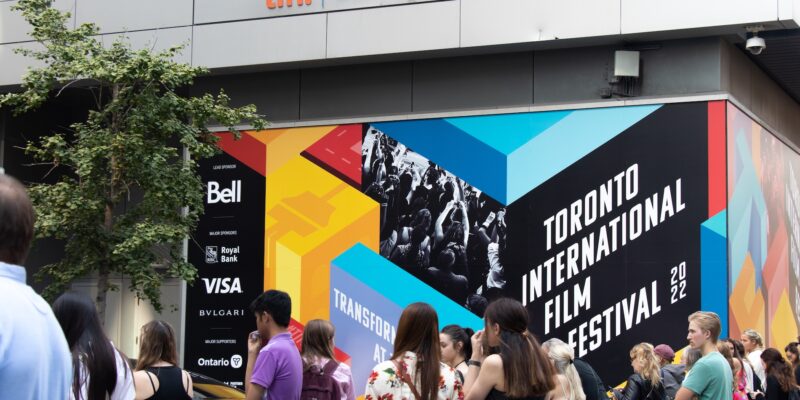 Toronto, ON, Canada - September 9, 2022: A crowd outside of the main celebrity entrance at TIFF, the Toronto International Film Festival, next to a colourful poster in the background.