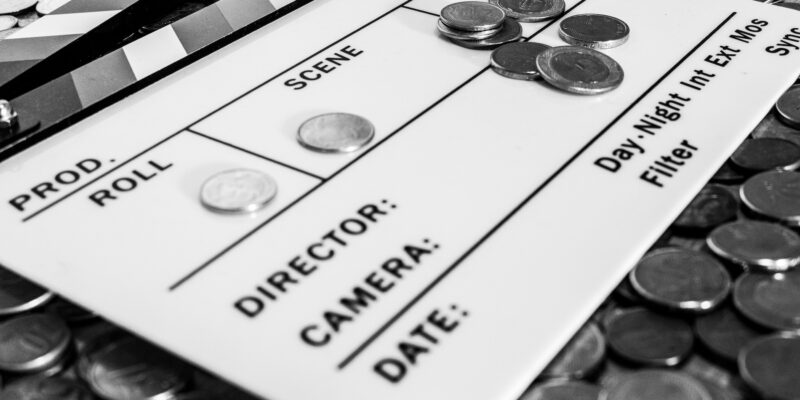 Clapperboard with coins above and on it creating a relation between filmmaking and business [Black and White version]