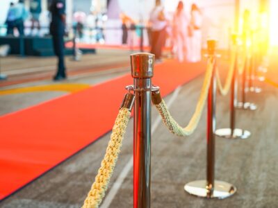 Wide panoramic view rope fencing with gold pillars with a red carpet for celebrities and guests of an expensive event with crowds of people
