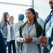 Group of diverse business professionals, businessmen and businesswomen, networking at a conference event. They are smiling, conversing, and engaging in discussions during a daytime seminar.