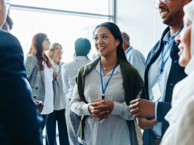 Group of diverse business professionals, businessmen and businesswomen, networking at a conference event. They are smiling, conversing, and engaging in discussions during a daytime seminar.