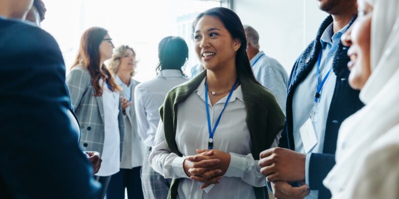 Group of diverse business professionals, businessmen and businesswomen, networking at a conference event. They are smiling, conversing, and engaging in discussions during a daytime seminar.