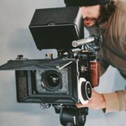 A young male cameraman behind a movie video camera filming on set