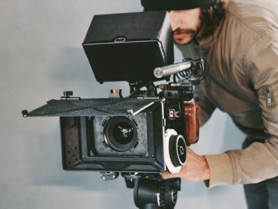 A young male cameraman behind a movie video camera filming on set