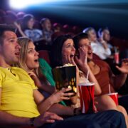 Audience sitting in multiplex movie theater, watching horror movie, screaming.
