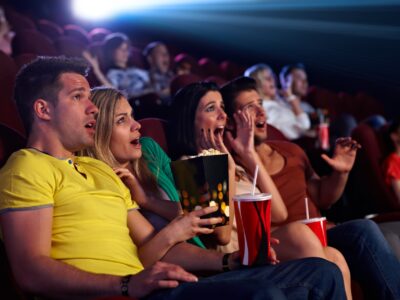 Audience sitting in multiplex movie theater, watching horror movie, screaming.