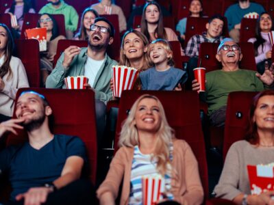 A young adult mother and father are in a movie theater with their small child enjoying a movie together over the weekend.