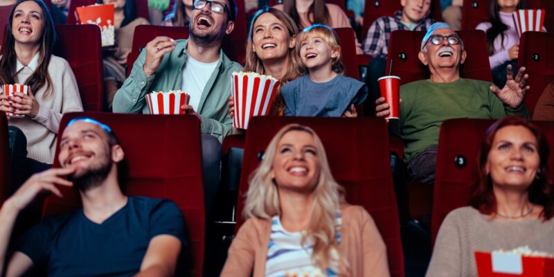 A young adult mother and father are in a movie theater with their small child enjoying a movie together over the weekend.
