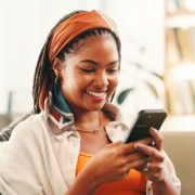 Smile, online and woman with smartphone in home for social media, reading forum or ebook. African person, mobile and relax on sofa with chat app for communication, text notification or download game