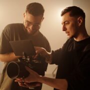 Waist up shot of two young male videographers reviewing footage on camera monitor during music video shoot in studio
