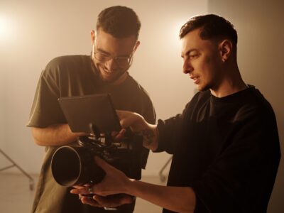 Waist up shot of two young male videographers reviewing footage on camera monitor during music video shoot in studio