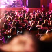 Spectators sit in the hall and watch a concert. People in the auditorium watching the performance. Theater audience. Music concert or festival. Out of focus.