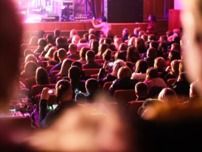 Spectators sit in the hall and watch a concert. People in the auditorium watching the performance. Theater audience. Music concert or festival. Out of focus.
