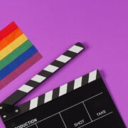 A rainbow flag and black clapperboard on purple background.