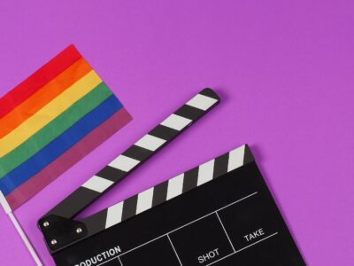 A rainbow flag and black clapperboard on purple background.
