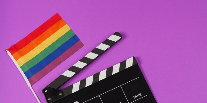 A rainbow flag and black clapperboard on purple background.